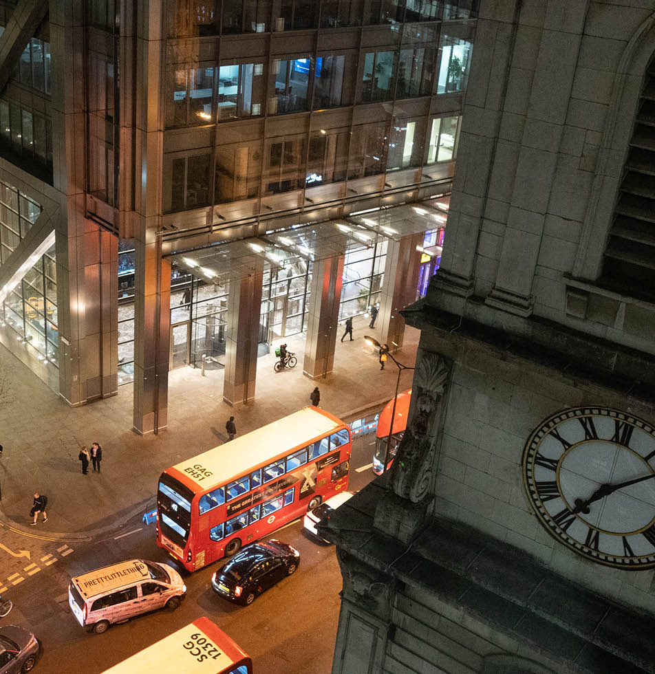 London at night with a red london bus on a road. There is a clock tower to the right of the screen which shows 25 to 2 